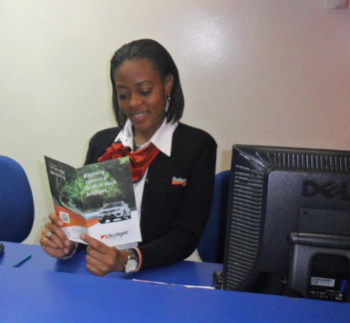 Budget Rent a Car Jamaica office with a woman sitting at a desk reading a brochure.