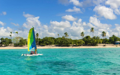 Ocean view from Bay Gardens Resorts in St. Lucia, showing a small sailboat on clear blue water with sand, green landscaping and blue skies.