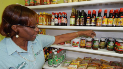 Barbados Agricultural Development Marketing Corporation. A woman reaches to a jar on a shelf in a store.