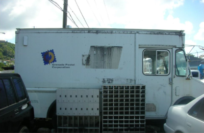 A Grenada Postal Corporation truck parked with two mail holders on the ground next to it.