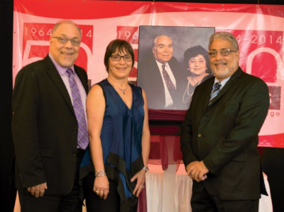 Abed and Company owners dressed up standing in front of a banner for the business's 50 year anniversary.