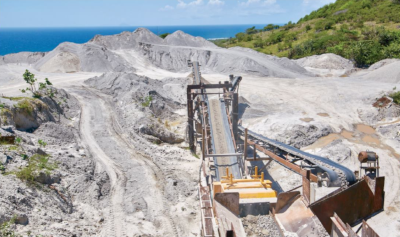 Lefco Equipment Rental. A mining excavator with a belt to move materials is at work with piles of earth in the background and the ocean.