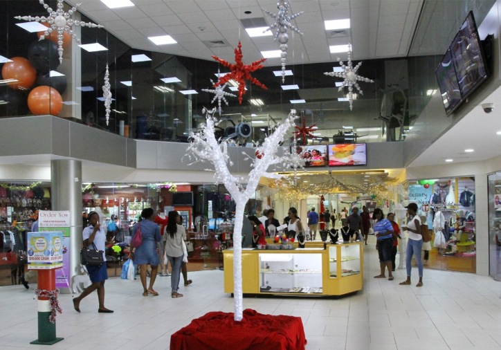 Sky Mall Barbados shopping mall view of a main walkway with two stories of shops in view. Winter Holiday decorations hanging from the ceiling and some at floor level.