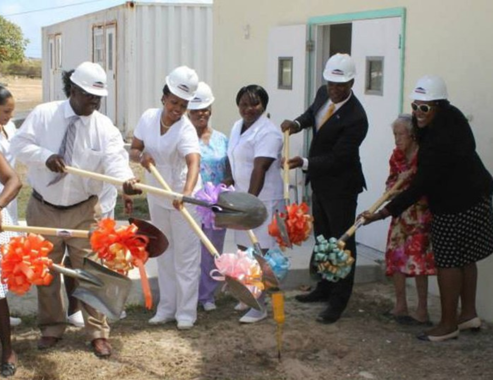 A group of people dressed up wearing hard hats using shovels with bows attached to break ground at a building.