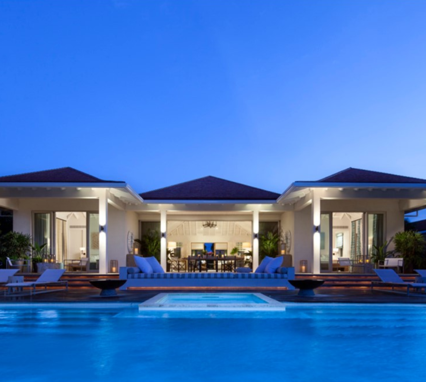 Blue sky, water and lighting of a back lanai view of a beautiful home at dusk with the inside lights on and lanai doors open. Project by Projetech Construction Management and Services.