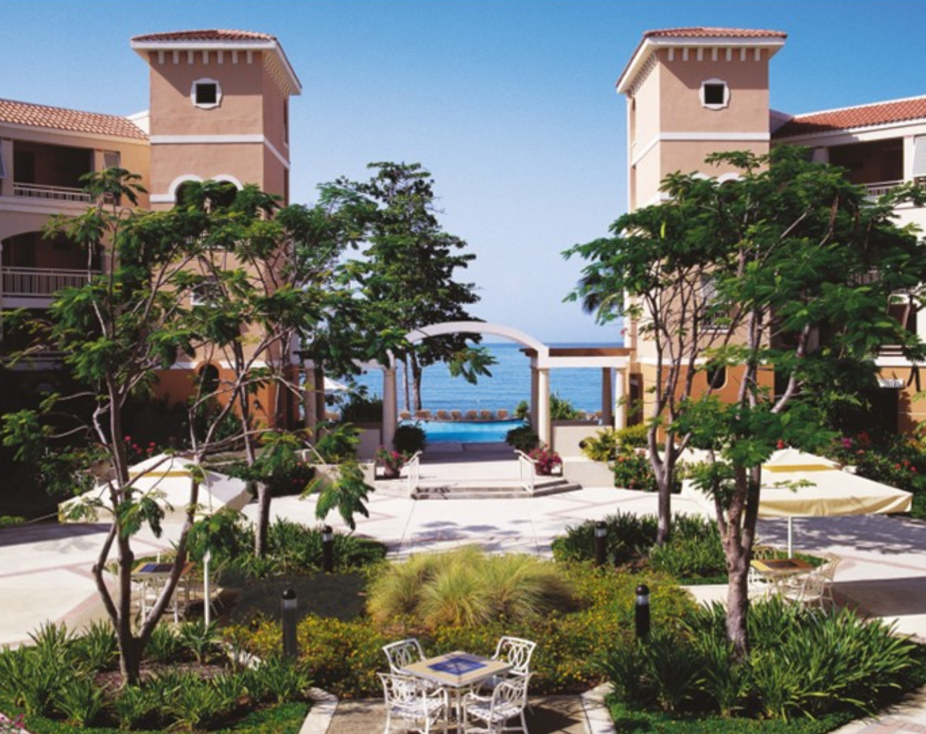 Outdoor patio view with a walkway around landscaping and a pool and ocean in the background at Rincon Beach Resort Puerto Rico.