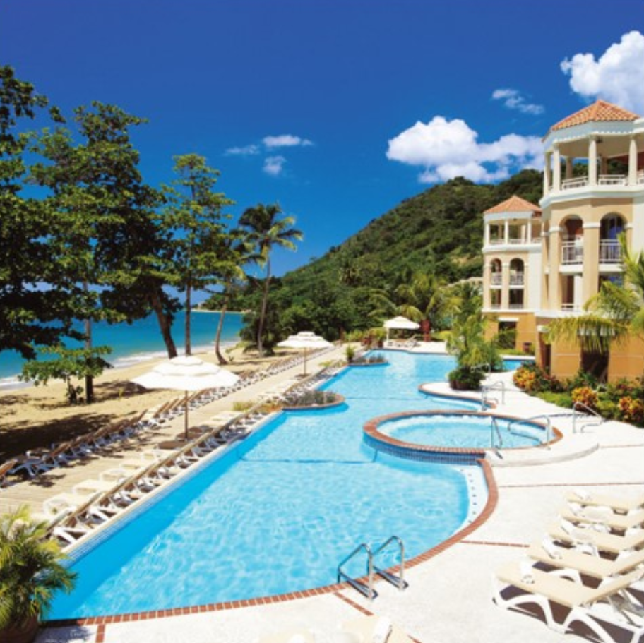 Outdoor side view of the Rincon Beach Resort's pool with the resort buildings on the right and beach on the left.