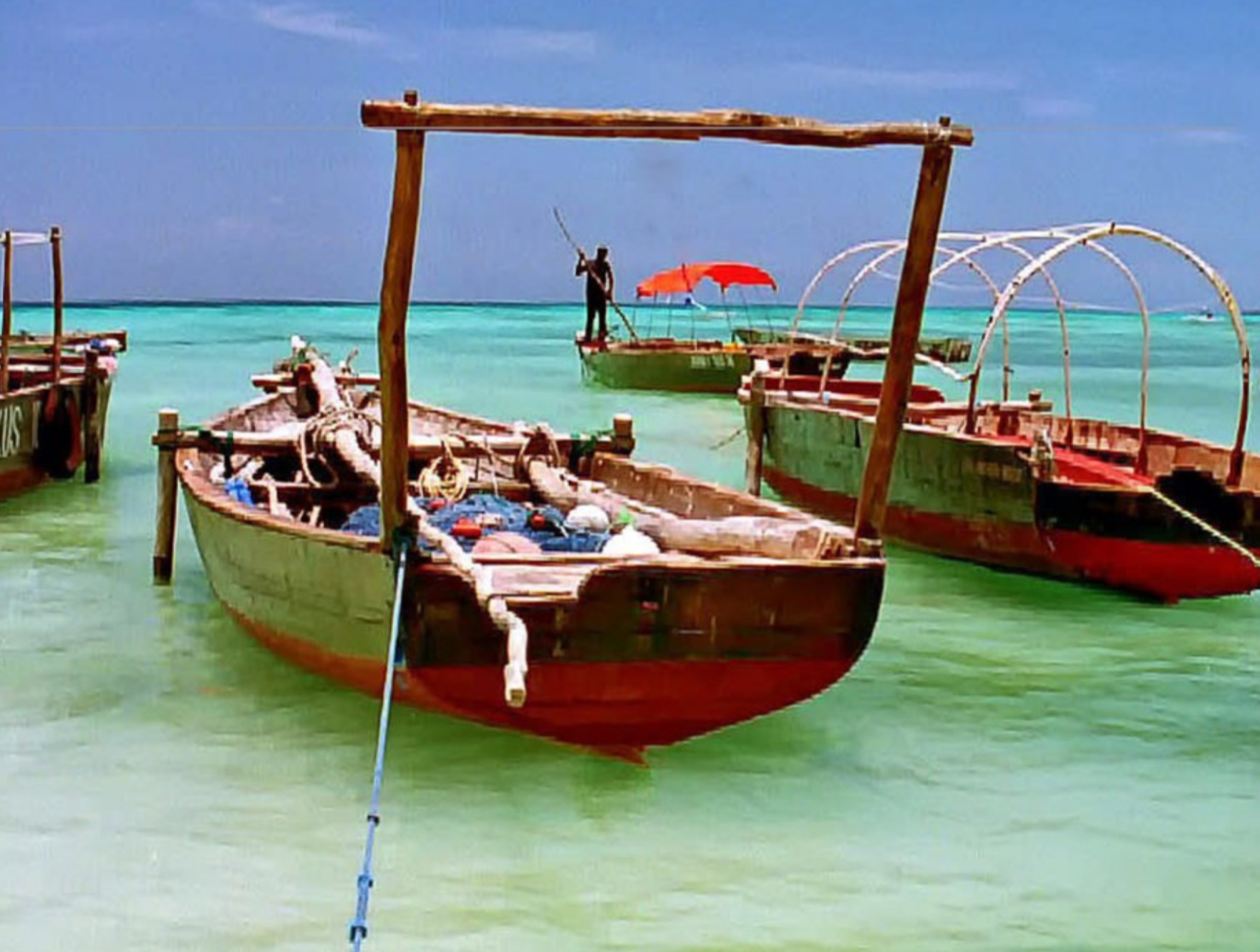 Wooden boats docked in the foreground with one being propelled by a pole in the background.