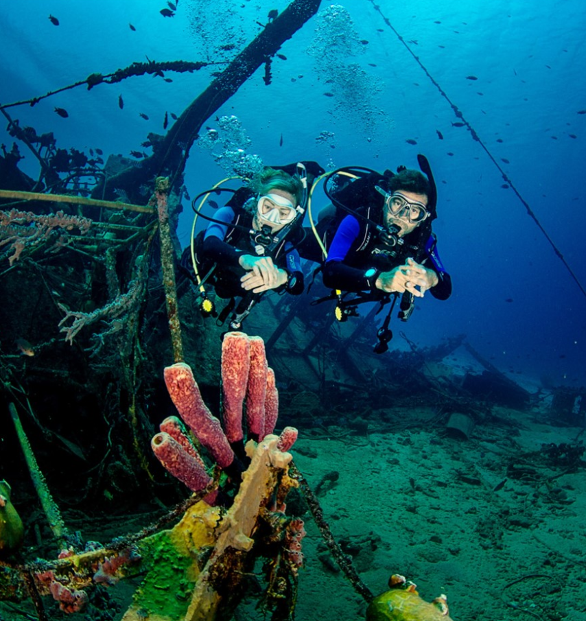 Scuba divers at harbour village beach club in blue water next to a ship wreck with coral.