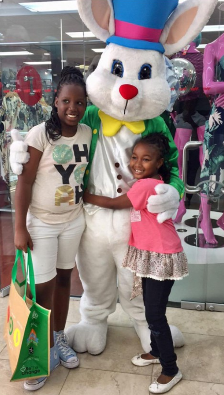 Children hugging and standing with the Easter bunny in front of a storefront at the mall