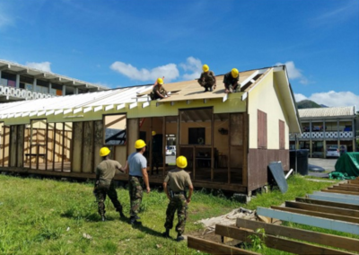 Construction workers putting in a roof on a build with 3 on the roof and 3 on the ground.