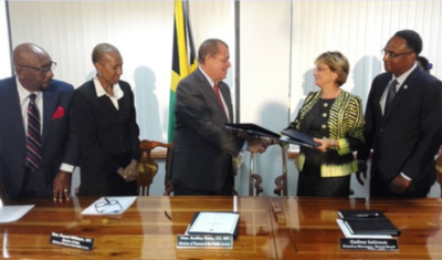 Minister Shaw shakes the hand of a woman at a meeting with others standing nearby.