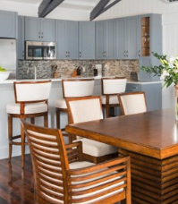 A Norstar Group home example show a kitchen in the background with wood accented stools at a bar and a nice wood dining table and chairs in the foreground.