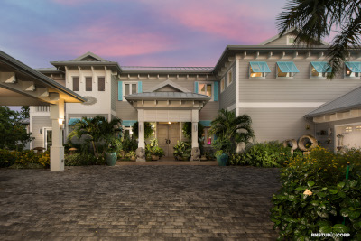 Yacht Drive Residence by Phoenix Construction. Great view on the front of a house with a custom brick driveway potted plants and other in ground landscaping on every edge of the house. Attached garage on the right with an open roof structure on the left.