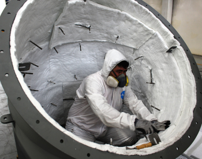 Equipos Inoxidables del Norte (Grupo ACV). A person working inside of a round metal object in a protective suit with respirator.