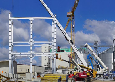 Incorporated Masterbuilders Association Jamaica construction site with a stationary crane and multiple vehicle cranes and workers putting up structures.