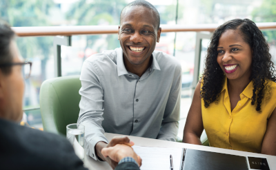 The University of the Commonwealth Caribbean. A man and woman sit at a desk with a man on the other side. The men are shaking hands.