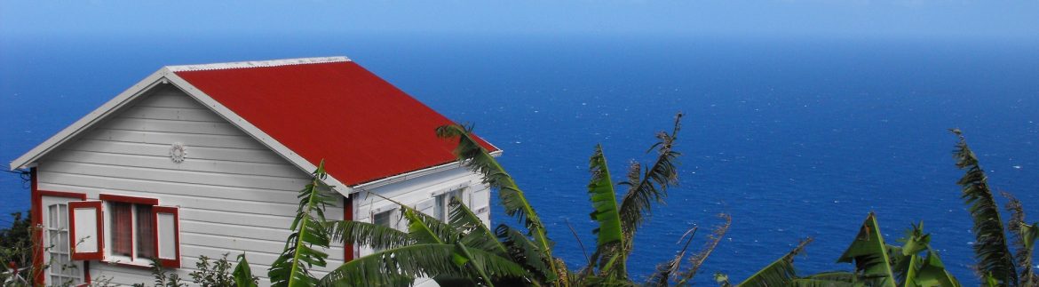 Zions Hills small red roofed house overlooking blue Caribbean water from a cliff.