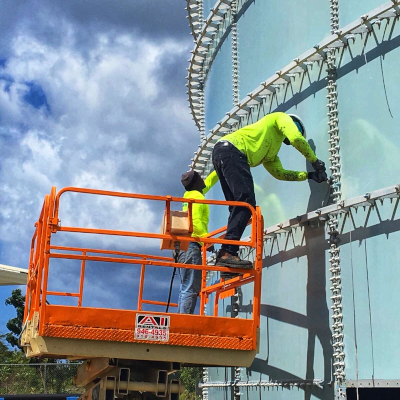 Two workers on a lift work on the outside of a metal water structure.