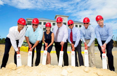 A row of seven people at a groundbreaking ceremony with shovels in the dirt.