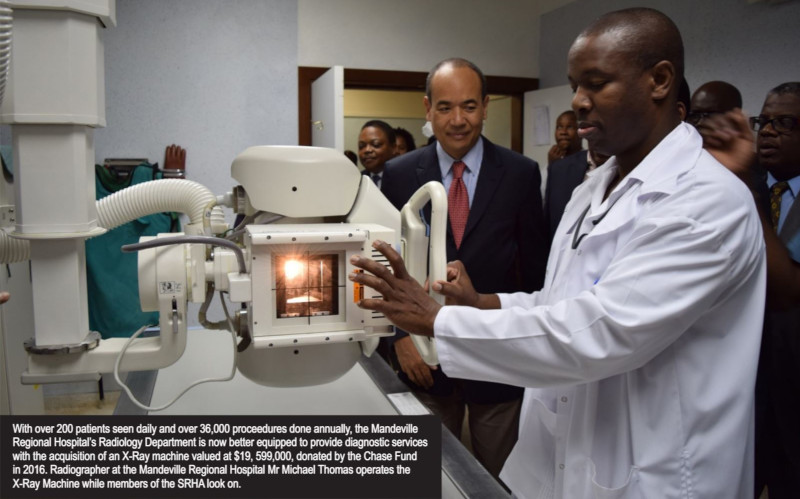 Southern Regional Health Authority - Jamaica. A man stand in front of medical equipment with people watching behind.