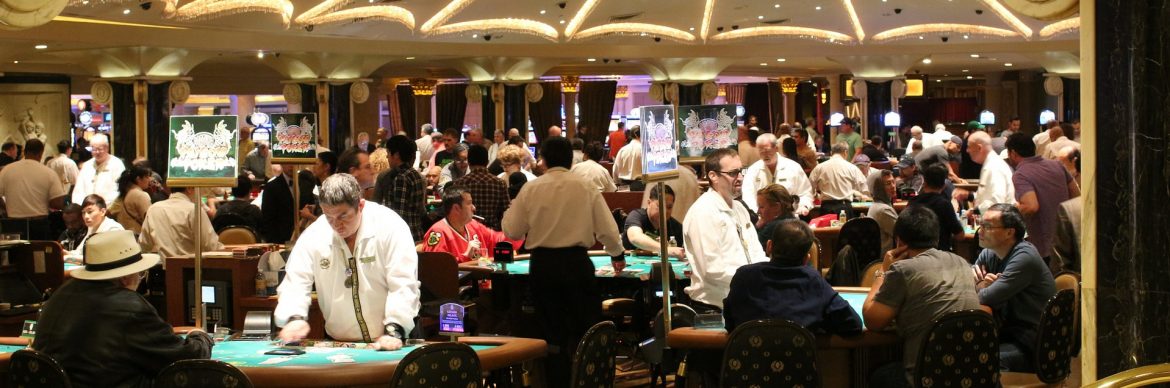 Casino floor tables with people gambling and dealers standing.