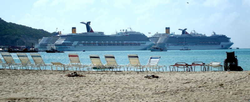St. Maarten Ministry of Tourism, Economic Affairs, Traffic & Telecommunication. Cruise ships in the background with a beach and lounge chairs in the foreground.