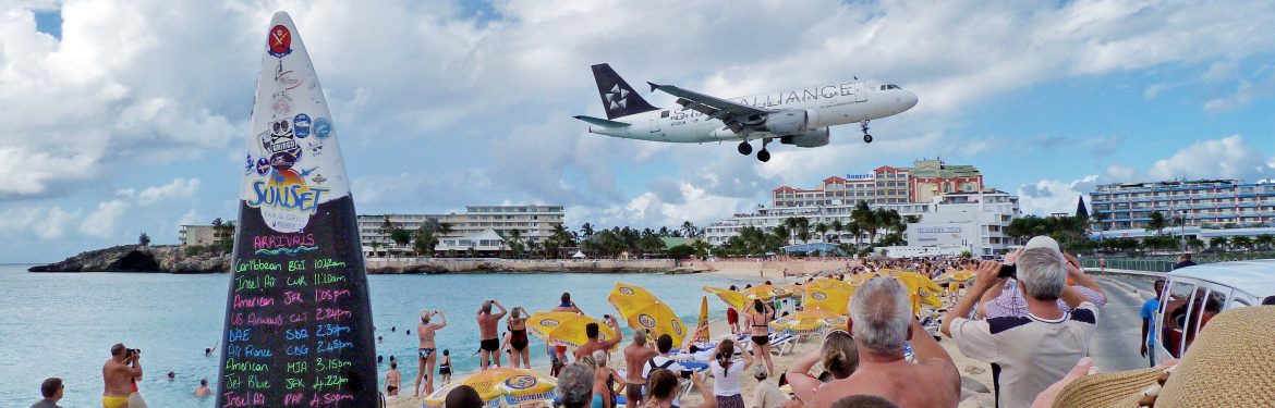 St. Maarten Ministry of Tourism, Economic Affairs, Traffic & Telecommunication. Commercial jet landing, coming in close to the beach before the runway with tourists taking photos.