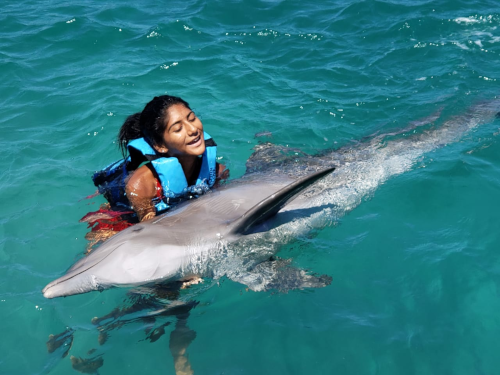 Puerto Seco Beach woman playing with a dolphin in the water with the Dolphin on its side.