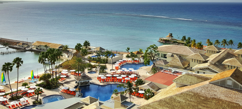 Moon Palace Jamaica, aerial view of the property with palm trees and the ocean stretching to the horizon.