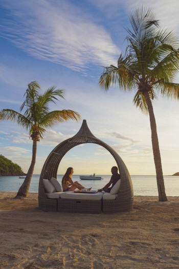 Carlisle Bay Resort Antigua couple sitting on a wicker chair with cushions on the beach.